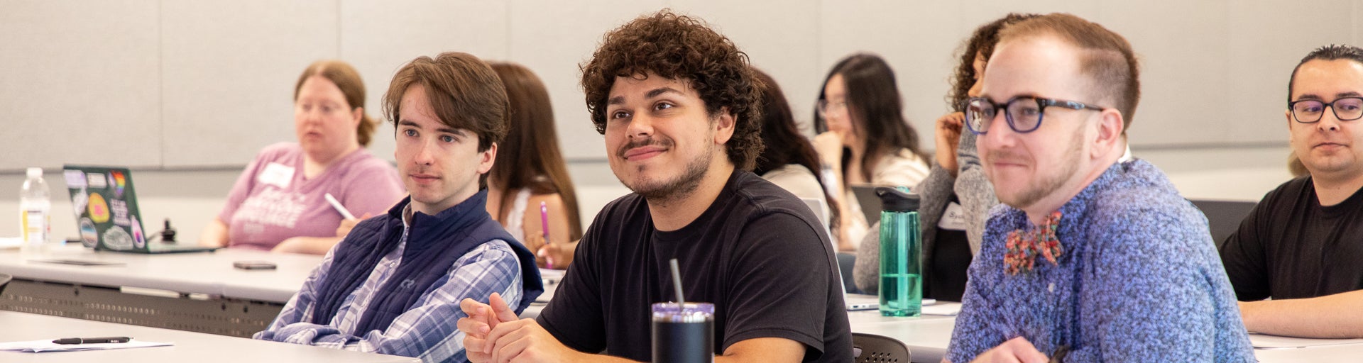 Three students sitting in an ASU Law classroom smiling while watching the front of the class.