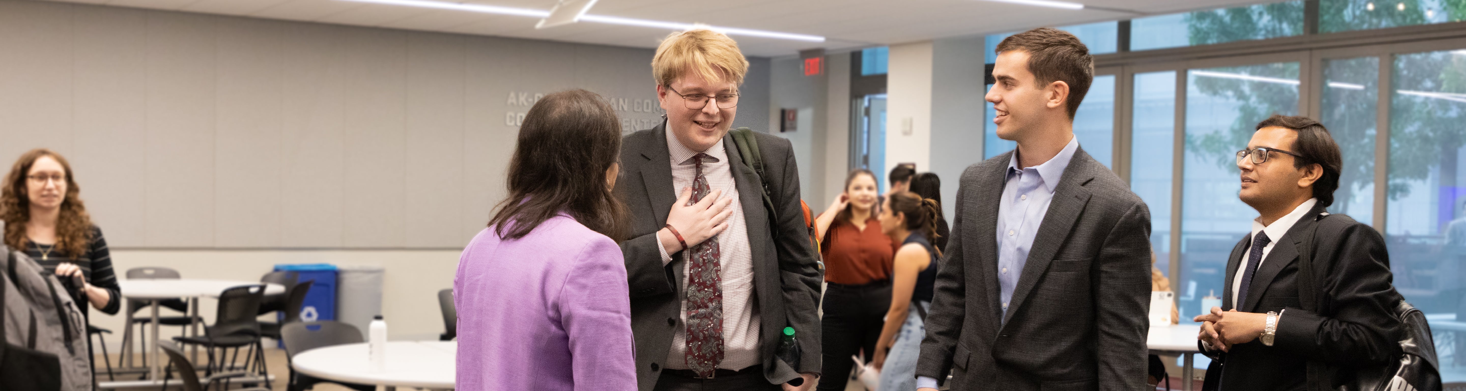 Three students in gray business suits talking to Federal Trade Commissioner, Chair Lina M. Khan in an ASU Law classroom.