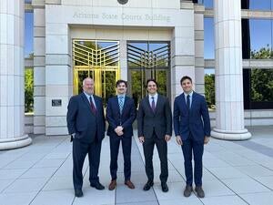 Four men in suits pose outside of a courthouse.